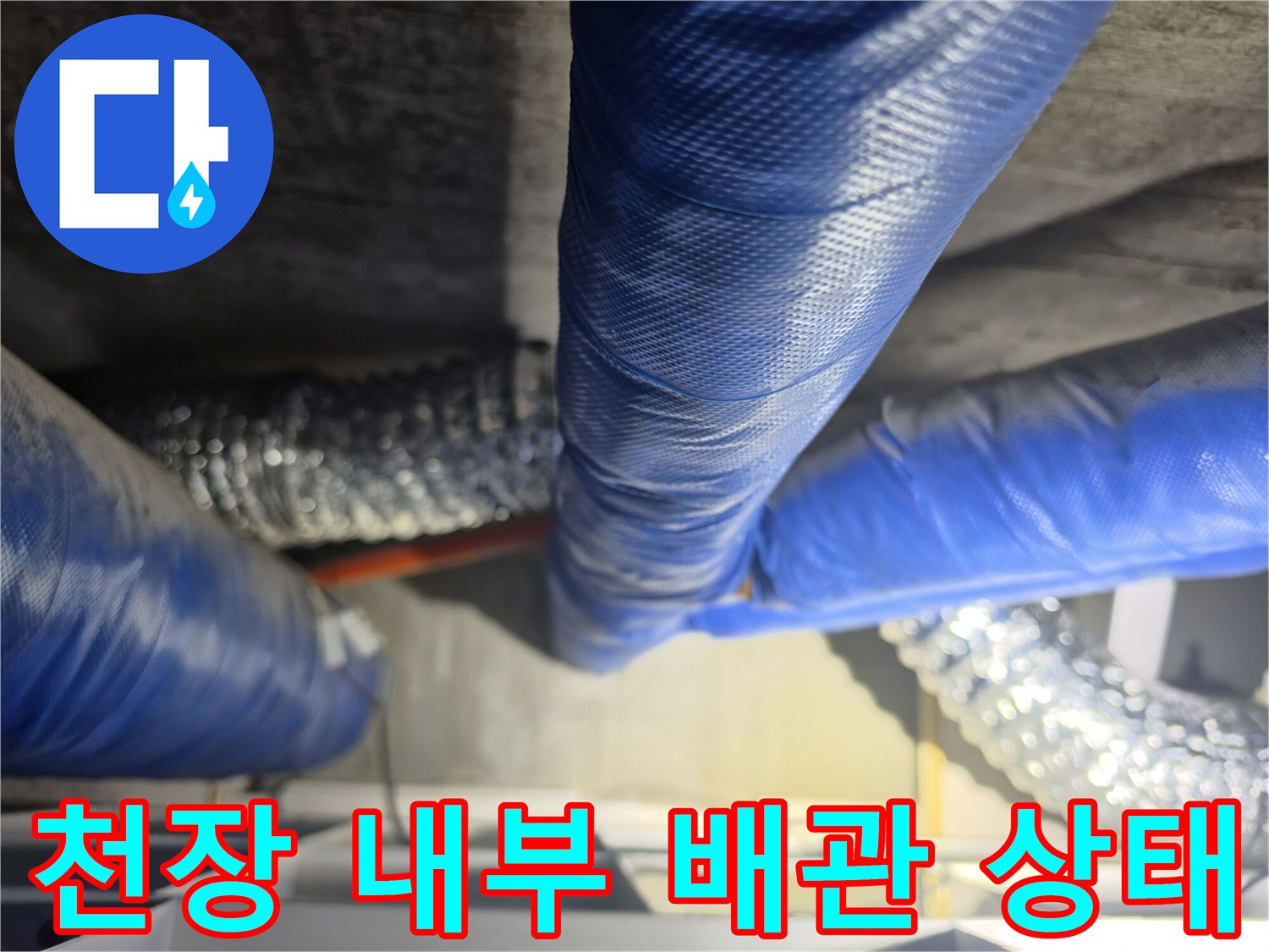 파란색 배관 보온재와 은색 자바라 호스가 얽혀 있는 천장 구조물 사진