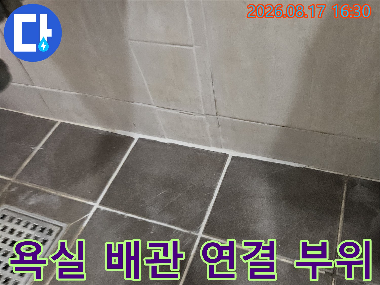 세면대 하부-금속 배관과 어두운 타일 바닥