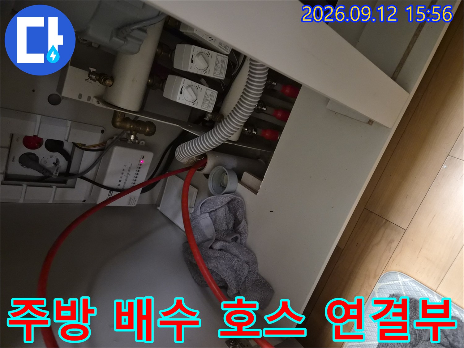 싱크대 하단에 위치한 주름진 배수 호스와 급수 밸브의 모습